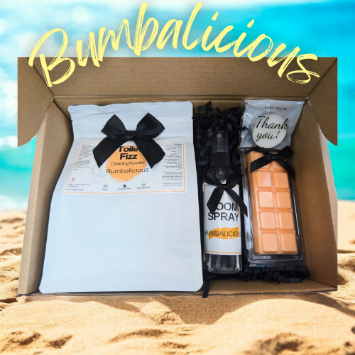 A brown gift box is opened to show the products from the Bumbalicious Home Box. The box sat on sand with a blue background