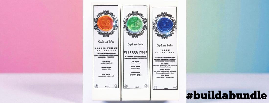 3 white perfume gift boxes lined up next to each other with matching black ribbons tied around their middle. The background is a backdrop of different shades of pale blues