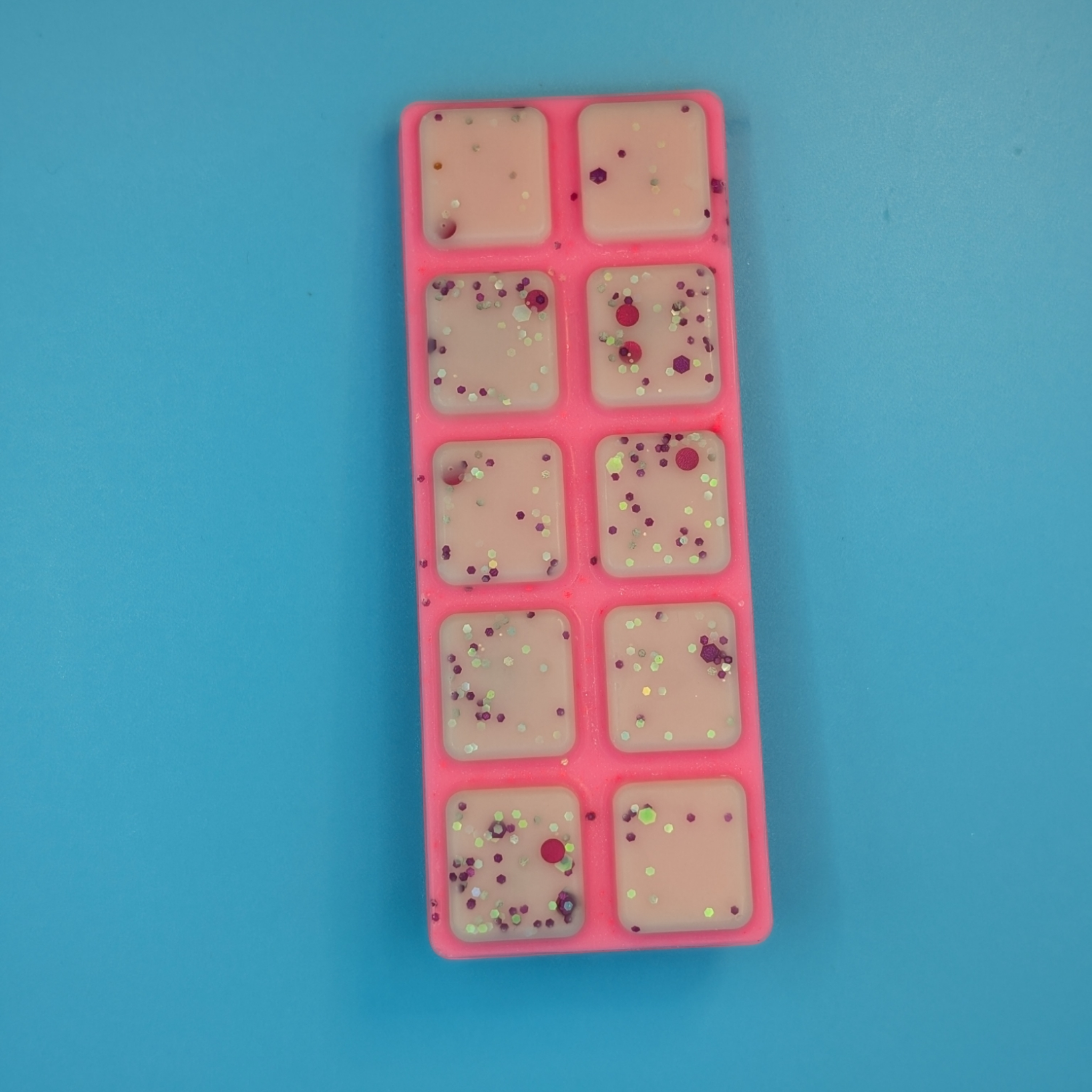 A pink par of ATHENA soy wax, with baby pink with glitter in segments on the bar.  The product is positoned on a blue background 