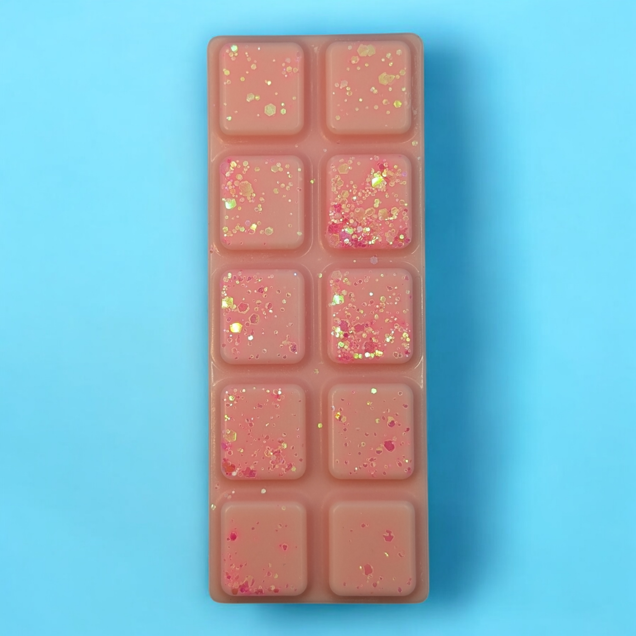 Baby pink soy wax melt bar, with big and small pieces of glitter on top.  The background is bright blue