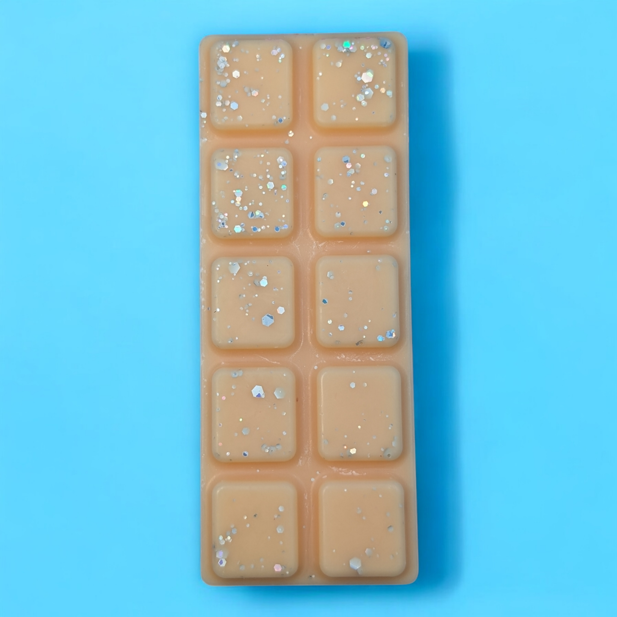 An orange wax bar with large and small pieces of glitter are scattered on top. The bar is on a blue background