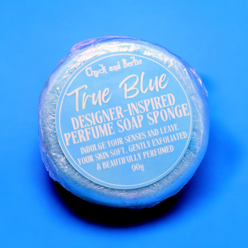 Round baby blue coloured sponge in cellophane wrap with a blue and white simple and clean designed sticker that says "Indulge your senses and leave your skin soft. Gently exfoliated and beautifully perfumed. 90 grams in weight." The background is the same shade of blue